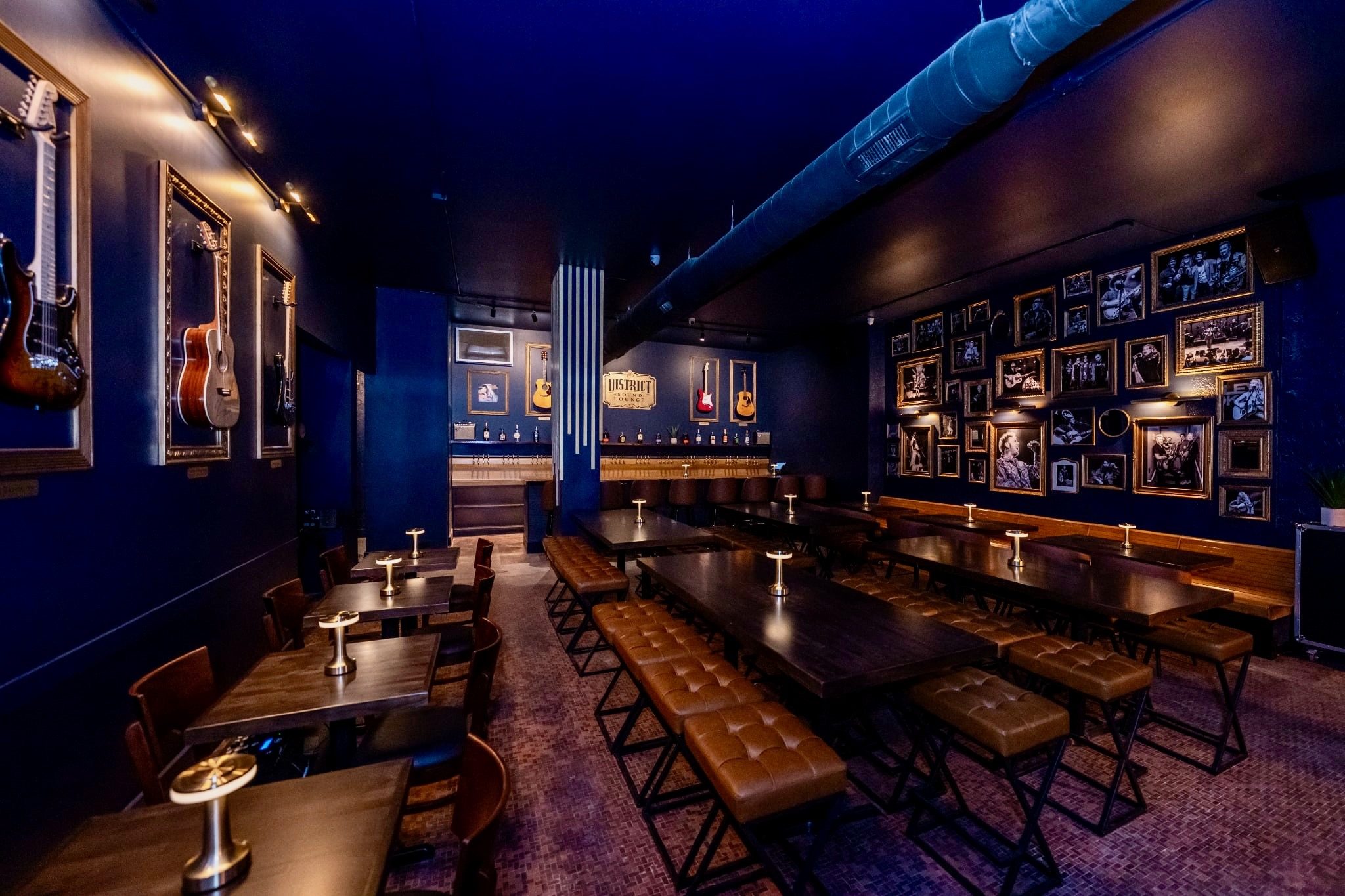 The main room of District Sound Lounge with framed guitars, a photo wall and long tables