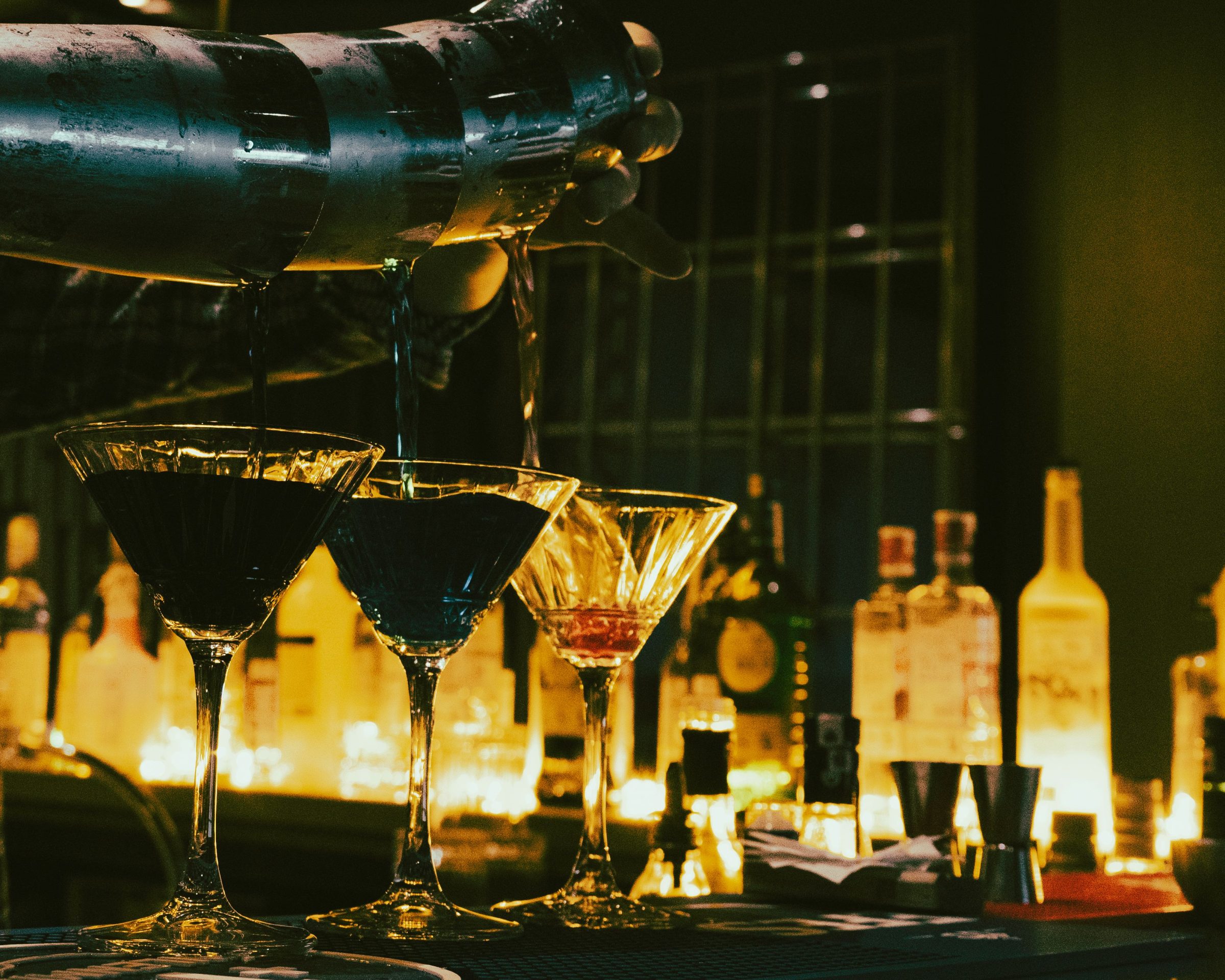 Glasses lined along a warmly lit bar with bottles behind